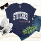 Navy t-shirt with distressed white varsity lettering spelling STITCHES arched across the chest, styled flat lay with sneakers and jeans