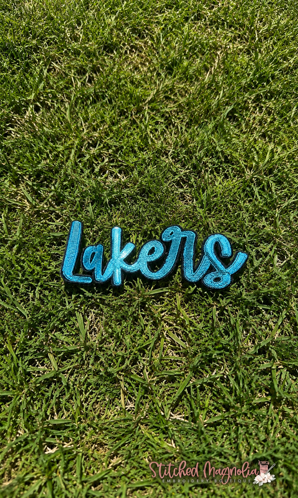 Mandeville Lakers teal embroidered patch on grass — Stitched Magnolia
